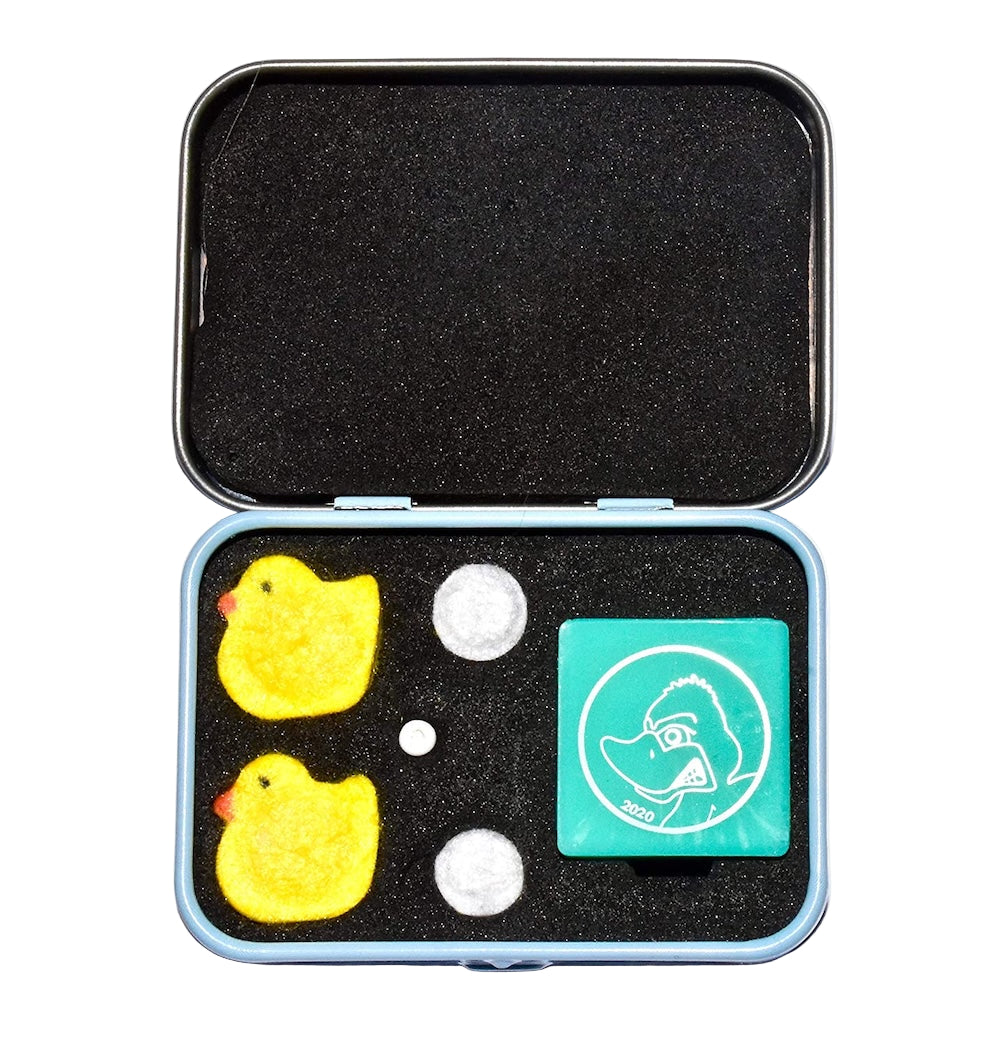 Two yellow rubber duckies, two white buttons, and a teal card with a duck illustration in an open black container.