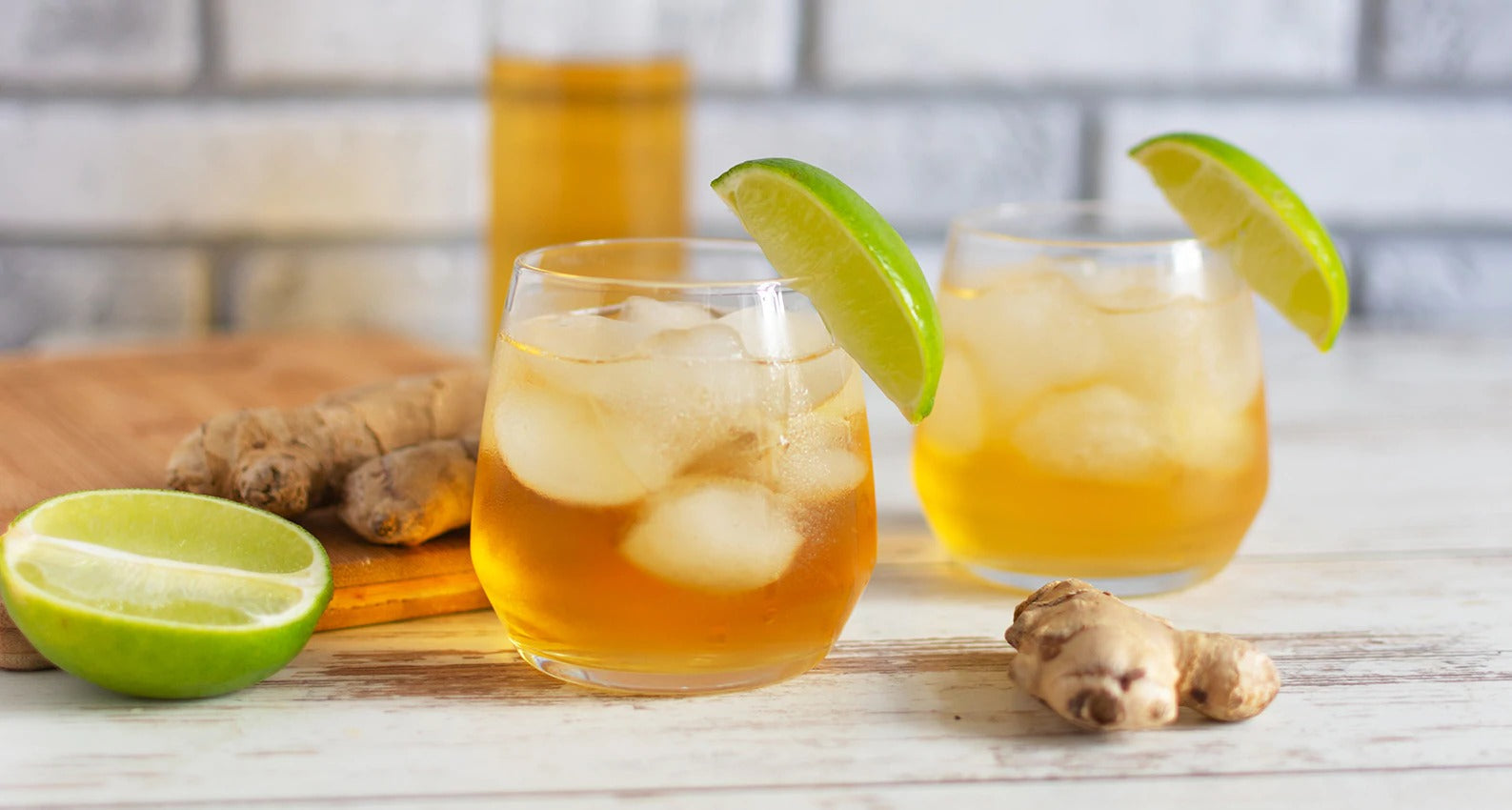 Two glasses of poured Detoxify Mega Clean Drink on a counter with ginger and lime slices.