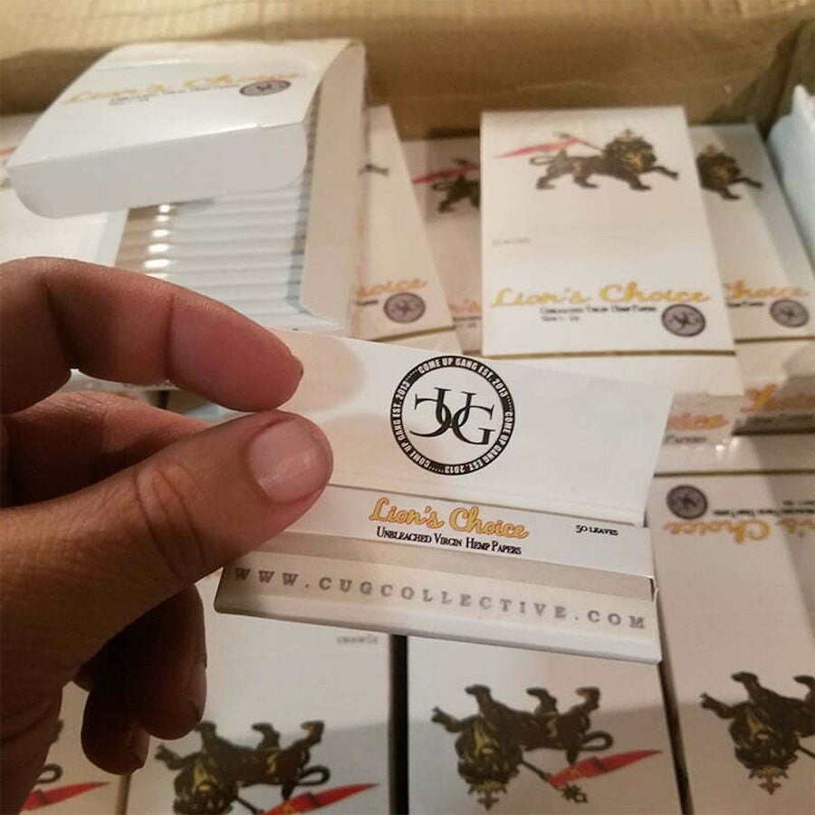 Hand holding a box of 'Lion's Choice' by CUG Collective with multiple boxes in the background.